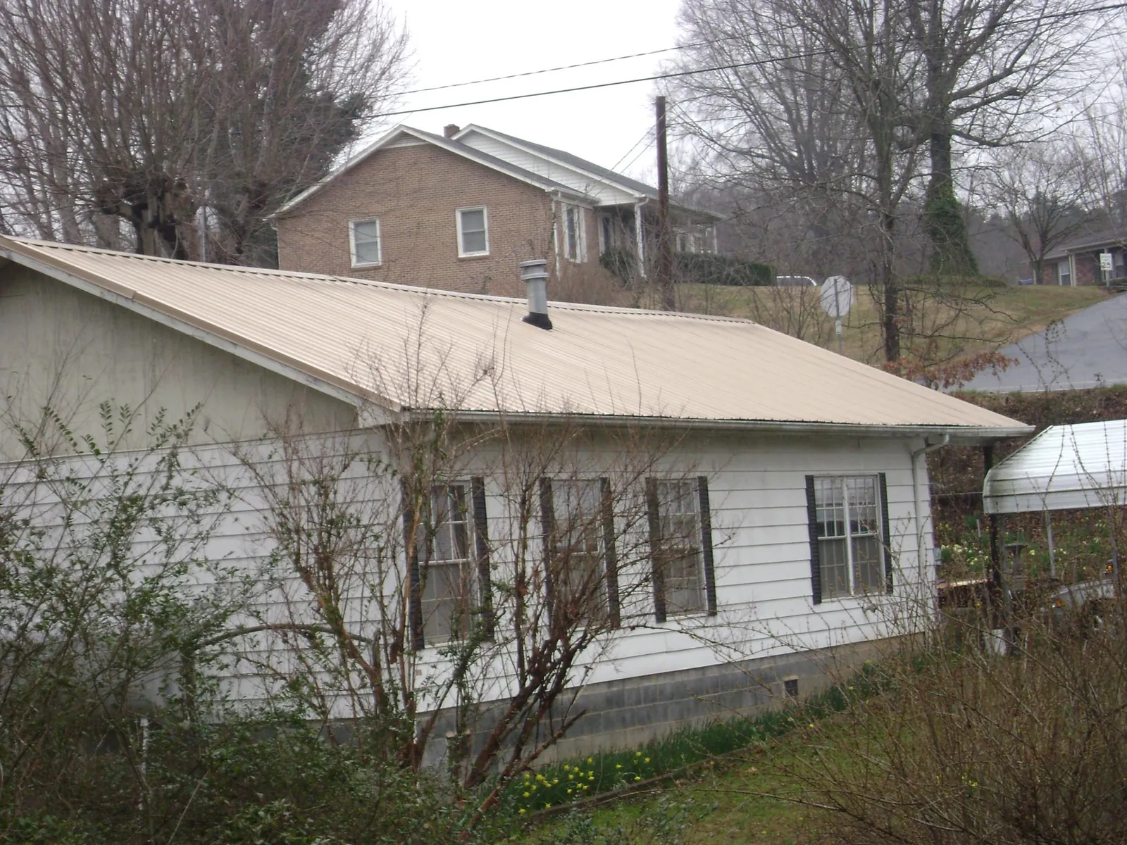 Tan metal roof on a white sided house set into a hillside — Commercial Roofing by Roofing Brothers in Martinsburg